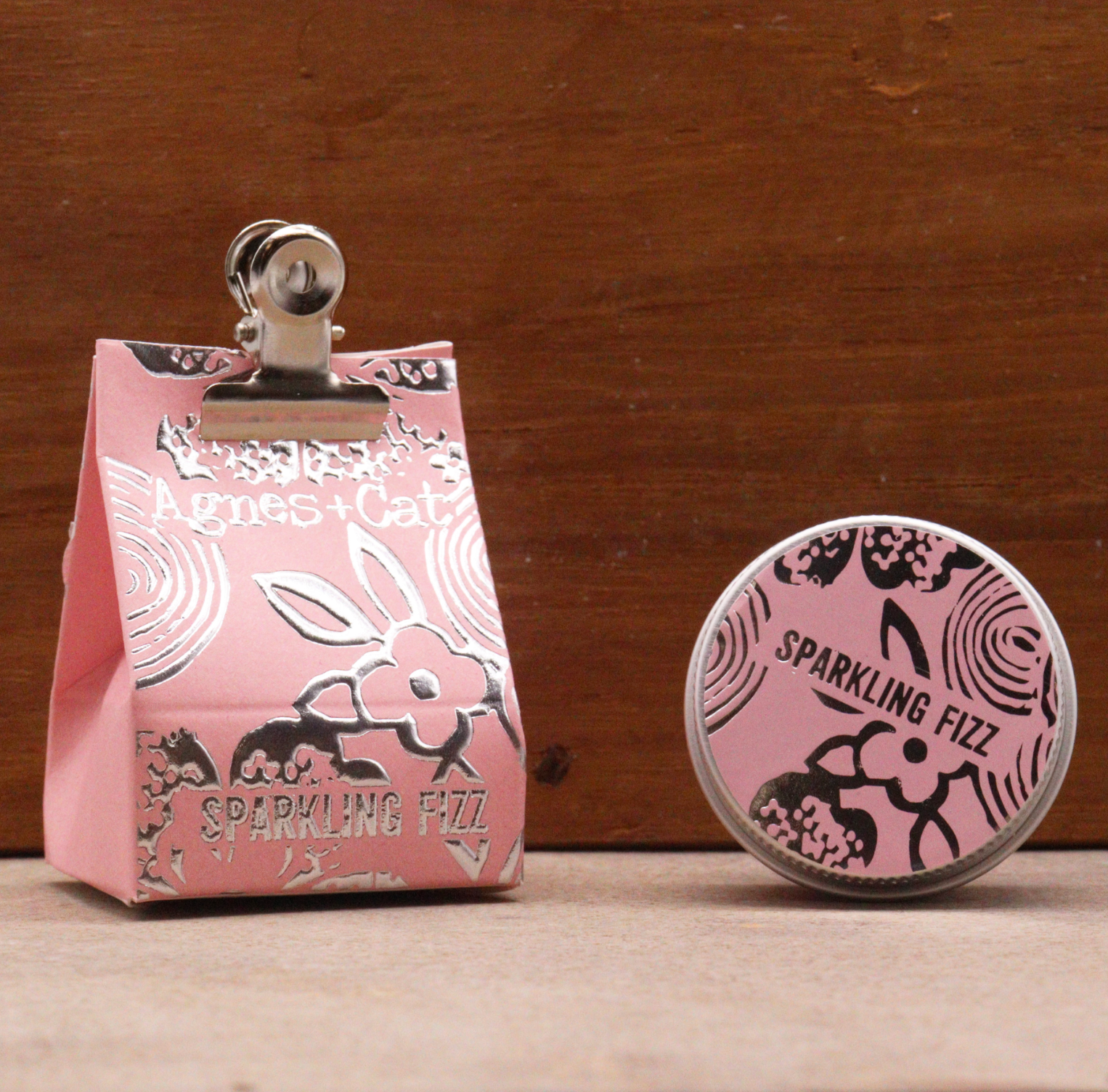 Pink packaged lip balm with a clip and 'Sparkling Fizz' branding on a wooden background