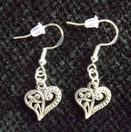 A pair of silver filigree heart dangle earrings with fishhook backings, displayed on a textured black fabric background.
