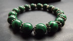 A beaded stretch bracelet made of polished green malachite beads with silver-toned spacer details, shown on a dark gray textured surface.