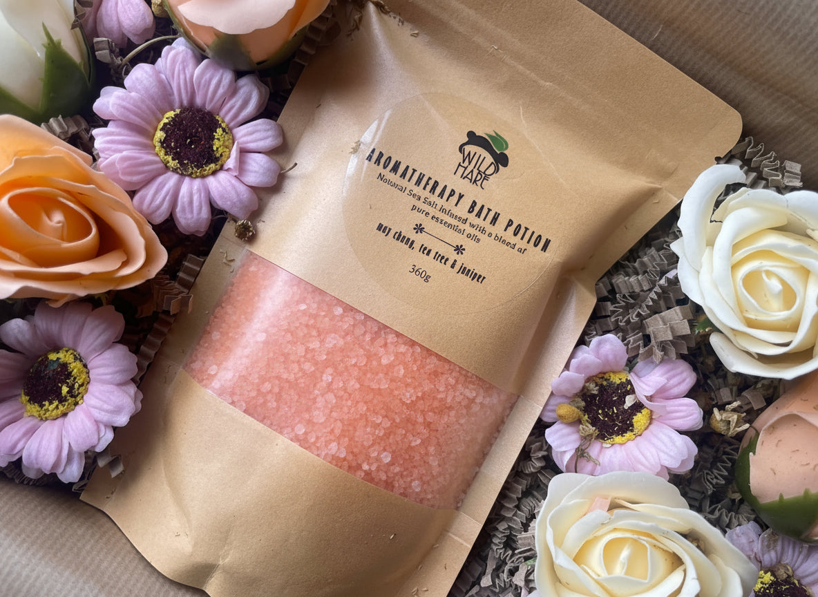 A package of aromatherapy bath potion surrounded by flowers on a textured surface.