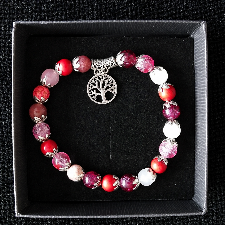 A beaded bracelet with red, pink, and white marbled beads and a silver tree of life charm, displayed inside a black presentation box on a black textured background.